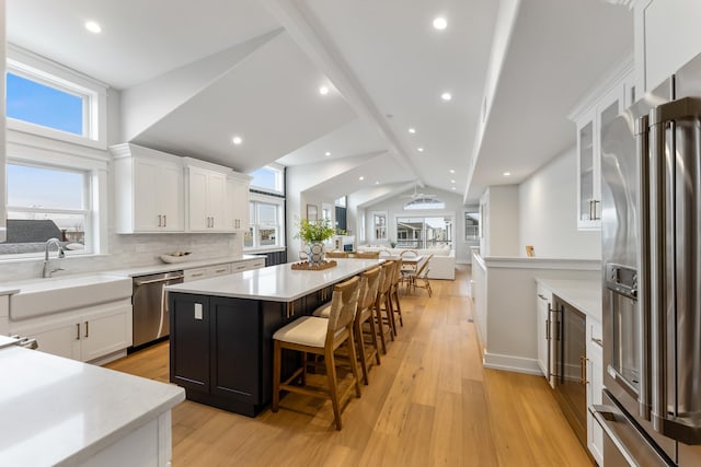 kitchen featuring vaulted ceiling, stainless steel appliances, a kitchen island, white cabinets, and a kitchen breakfast bar