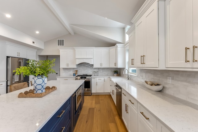 kitchen featuring stainless steel appliances, light stone countertops, blue cabinetry, and white cabinetry