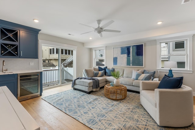 living room featuring wet bar, light hardwood / wood-style flooring, beverage cooler, and ceiling fan