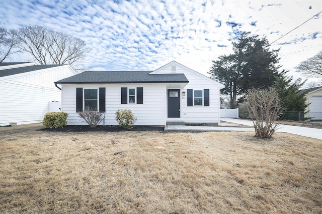 ranch-style home with roof with shingles, fence, and a front yard