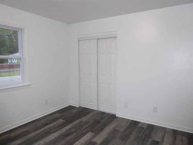 unfurnished bedroom with dark wood-style floors, a closet, and baseboards