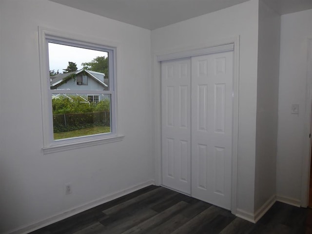 unfurnished bedroom featuring a closet, dark wood-style flooring, and baseboards