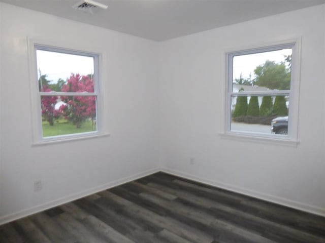 empty room with dark wood-type flooring, plenty of natural light, visible vents, and baseboards