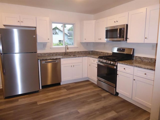 kitchen with appliances with stainless steel finishes, dark wood-type flooring, white cabinets, a sink, and dark stone countertops