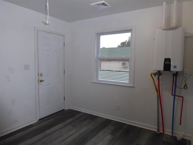 spare room with dark wood-style flooring, tankless water heater, visible vents, and baseboards