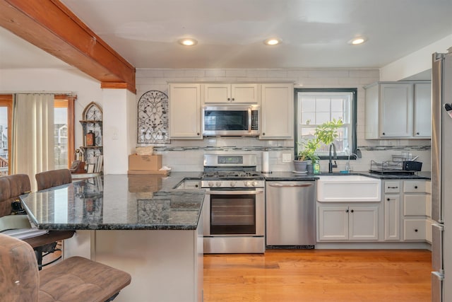 kitchen featuring tasteful backsplash, sink, dark stone counters, stainless steel appliances, and light wood-type flooring