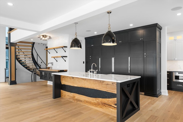 kitchen featuring light stone countertops, light wood-type flooring, a large island with sink, decorative light fixtures, and oven