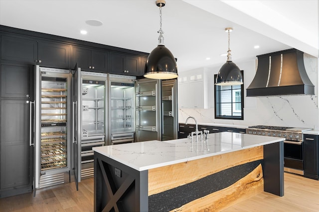 kitchen with light stone countertops, high end stainless steel range oven, a large island, and custom exhaust hood