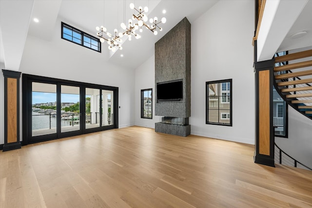 unfurnished living room featuring a fireplace, light hardwood / wood-style floors, a high ceiling, and an inviting chandelier