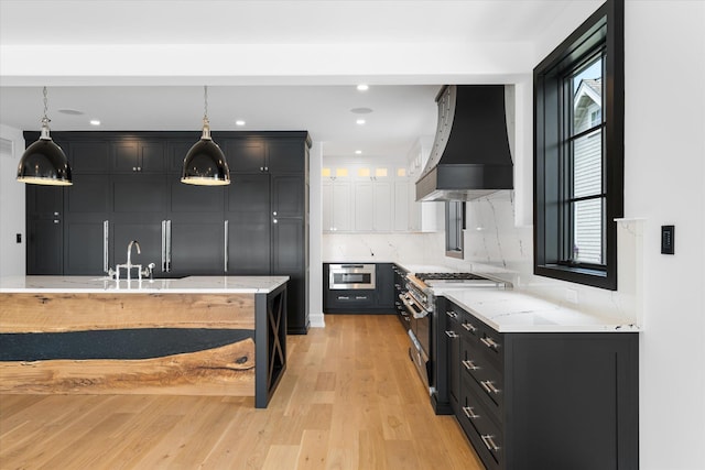 kitchen with custom exhaust hood, backsplash, gas range, light wood-type flooring, and decorative light fixtures