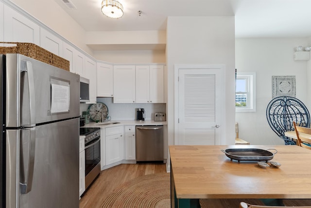 kitchen with stainless steel appliances, light wood-type flooring, white cabinets, and backsplash