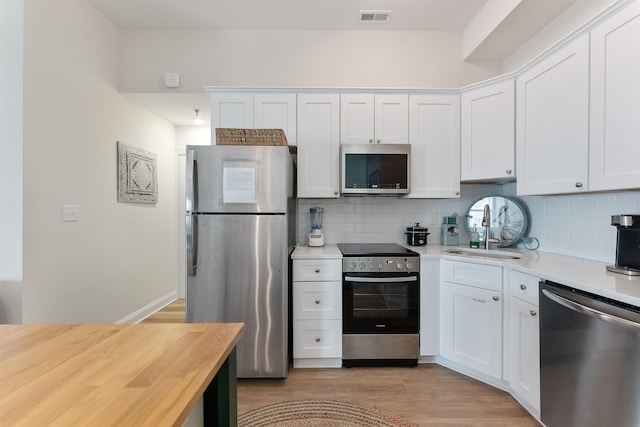 kitchen with appliances with stainless steel finishes, light wood-style flooring, backsplash, and visible vents