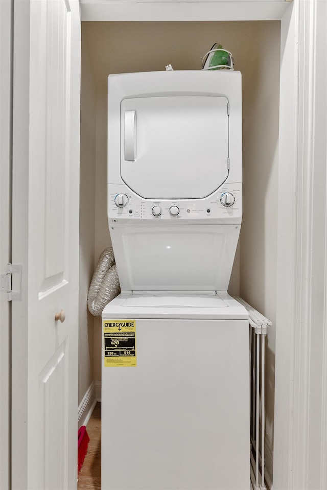 washroom with stacked washer and dryer, baseboards, laundry area, and wood finished floors