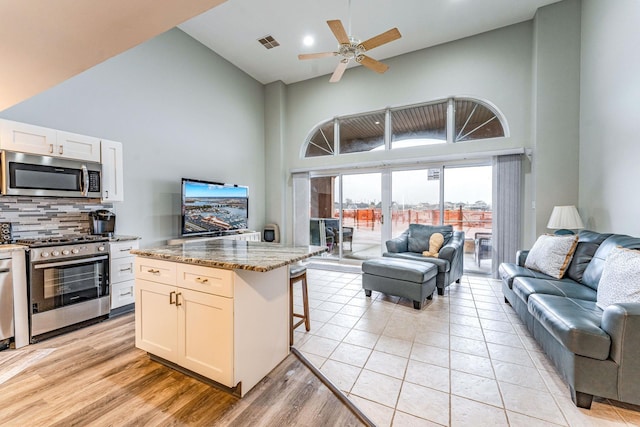 kitchen featuring stainless steel appliances, light stone counters, high vaulted ceiling, backsplash, and a breakfast bar area