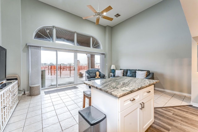 kitchen with a high ceiling, ceiling fan, light stone counters, a kitchen bar, and white cabinetry