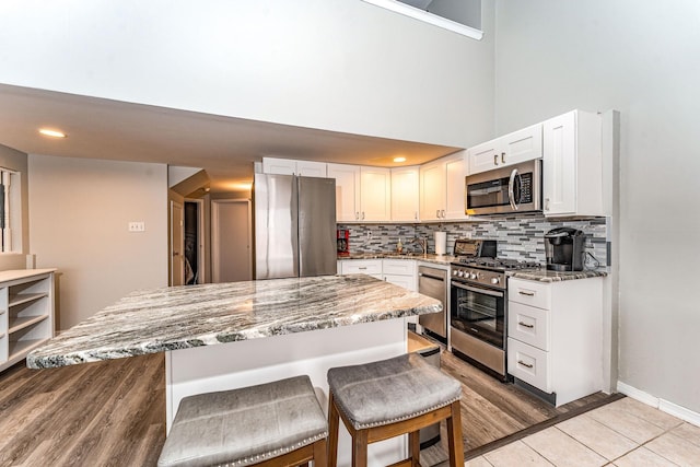 kitchen with white cabinetry, light stone countertops, a breakfast bar area, and stainless steel appliances