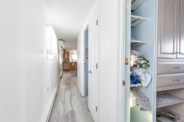 corridor with light wood-type flooring and an AC wall unit