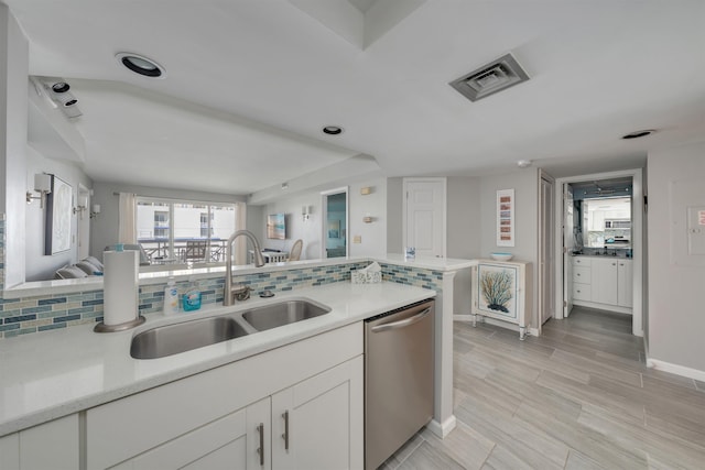 kitchen with white cabinets, stainless steel dishwasher, a sink, visible vents, and decorative backsplash