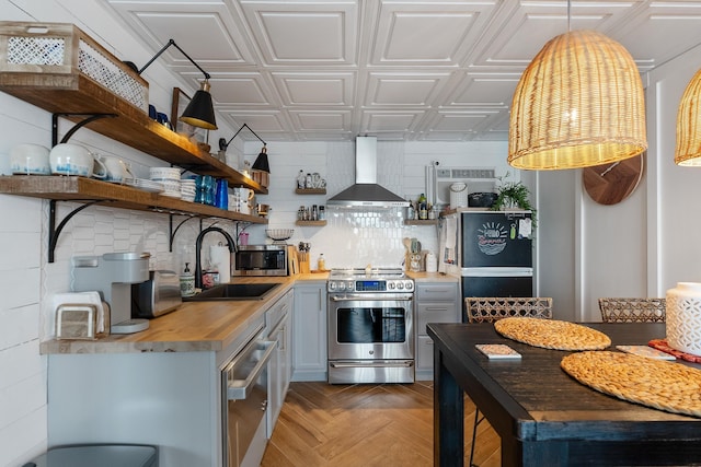 kitchen featuring butcher block counters, wall chimney range hood, sink, dark parquet flooring, and stainless steel appliances