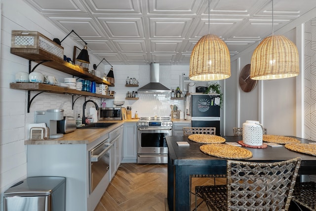 kitchen featuring appliances with stainless steel finishes, wall chimney exhaust hood, sink, butcher block countertops, and parquet flooring