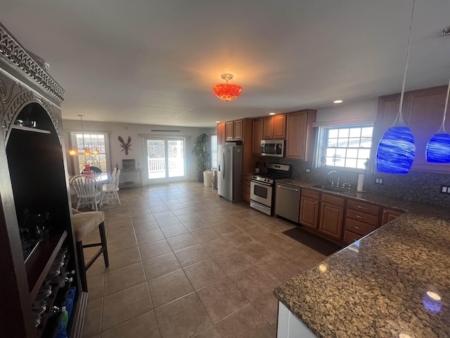 kitchen with sink, appliances with stainless steel finishes, hanging light fixtures, plenty of natural light, and dark stone counters