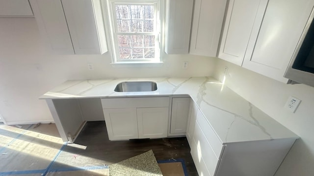 kitchen featuring dark wood-type flooring, a sink, white cabinetry, and light stone countertops