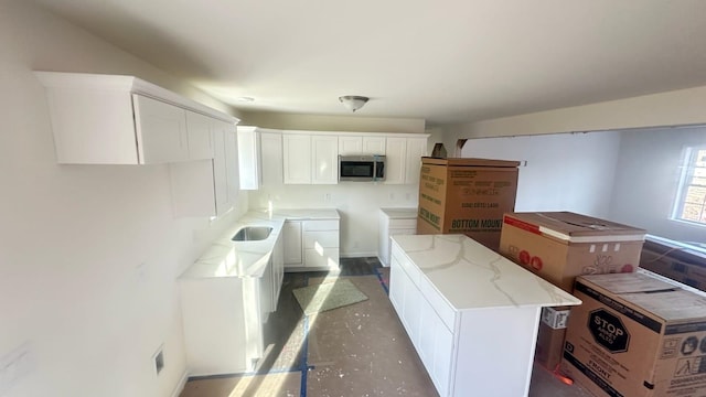 kitchen with concrete flooring, a kitchen island, visible vents, white cabinetry, and stainless steel microwave