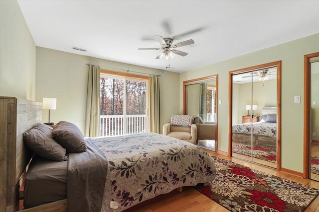 bedroom featuring two closets, visible vents, a ceiling fan, wood finished floors, and baseboards