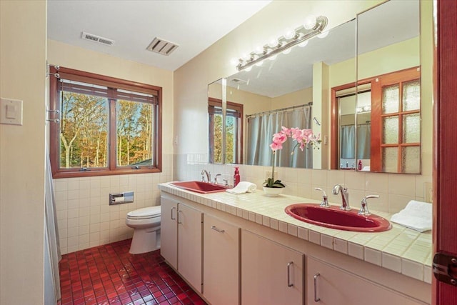 bathroom with a sink, visible vents, and tile walls