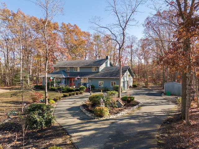 view of front of property with driveway, a chimney, a storage unit, and an outdoor structure