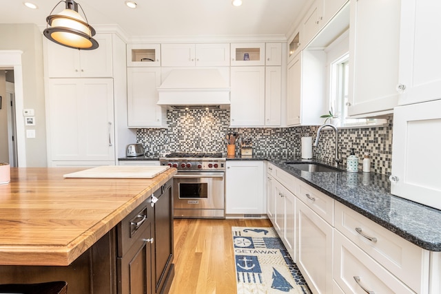 kitchen with premium range, a sink, white cabinets, and custom range hood