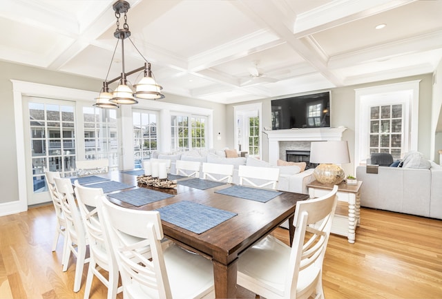 dining area with a fireplace, beamed ceiling, and light wood-style flooring