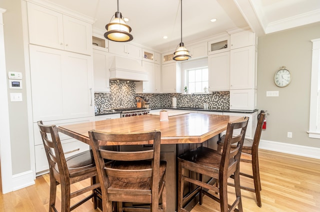 kitchen with light wood finished floors, a kitchen bar, decorative backsplash, and custom range hood