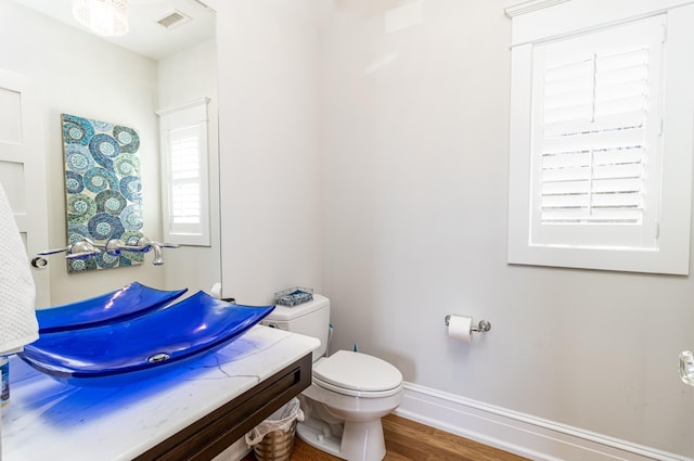 half bathroom with toilet, a sink, wood finished floors, visible vents, and baseboards