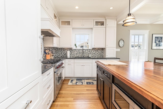 kitchen featuring stainless steel stove, custom range hood, wooden counters, a healthy amount of sunlight, and a sink