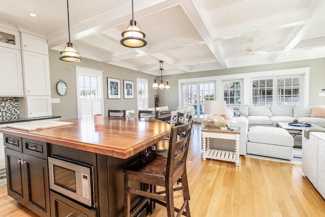 kitchen with stainless steel microwave, white cabinets, wood counters, light wood-type flooring, and a kitchen breakfast bar