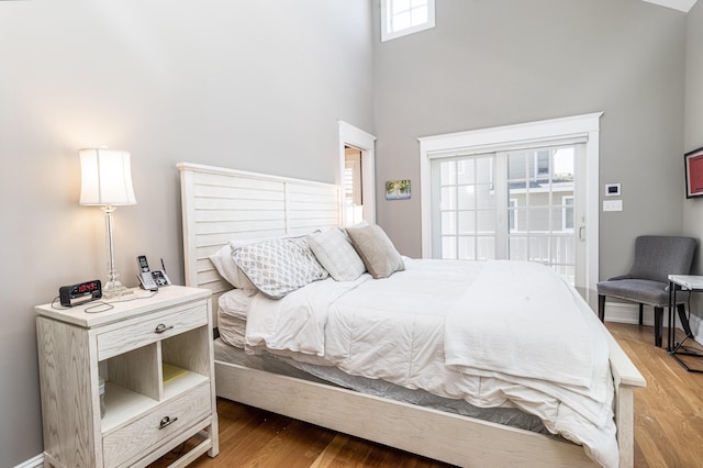 bedroom with a towering ceiling, access to exterior, light wood-style flooring, and baseboards