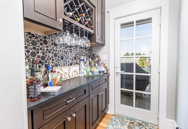 bar featuring light wood finished floors, a bar, and backsplash