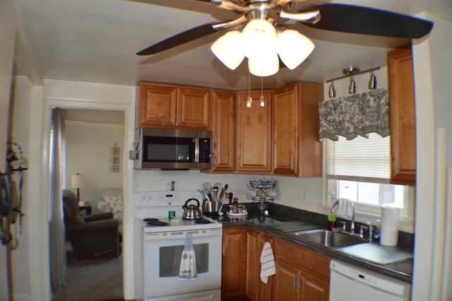 kitchen with brown cabinets, dark countertops, a ceiling fan, a sink, and white appliances