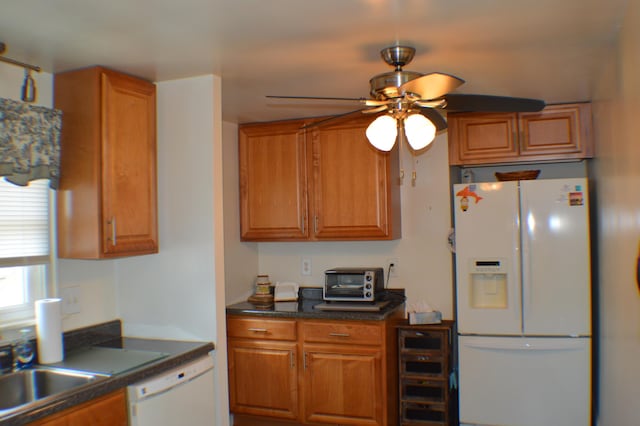 kitchen with brown cabinets, dark countertops, a sink, ceiling fan, and white appliances