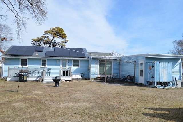 rear view of property featuring roof mounted solar panels and a yard