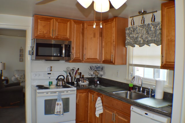 kitchen featuring brown cabinetry, dark countertops, white appliances, and a sink