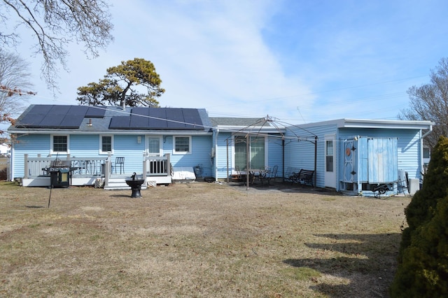 back of house featuring a yard, a wooden deck, and roof mounted solar panels