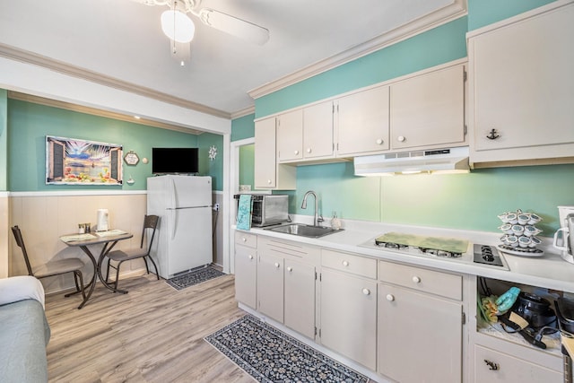 kitchen featuring freestanding refrigerator, a sink, under cabinet range hood, ornamental molding, and stovetop