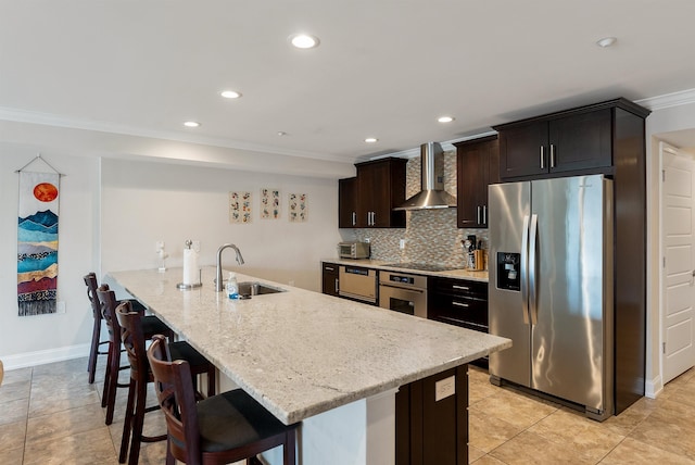 kitchen featuring sink, stainless steel appliances, wall chimney range hood, a breakfast bar area, and decorative backsplash