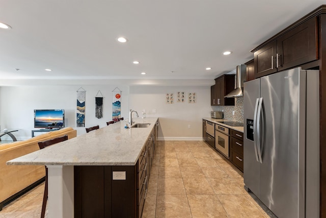 kitchen with a kitchen breakfast bar, sink, wall chimney exhaust hood, decorative backsplash, and appliances with stainless steel finishes