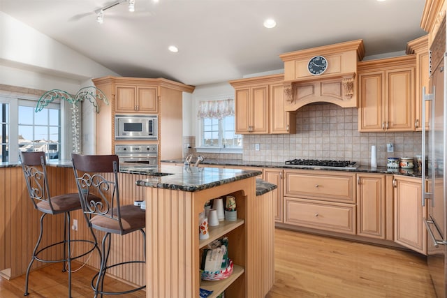 kitchen featuring light wood-type flooring, built in appliances, a center island with sink, and dark stone countertops