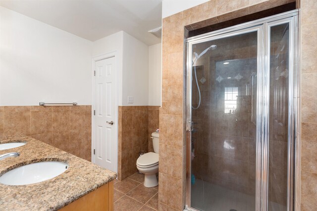 bathroom with tile patterned floors, vanity, tile walls, toilet, and a shower with shower door