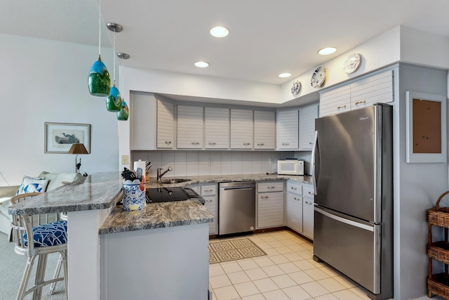 kitchen with backsplash, appliances with stainless steel finishes, decorative light fixtures, a kitchen bar, and kitchen peninsula