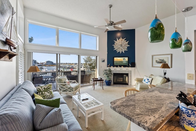 living room with ceiling fan, a towering ceiling, a textured ceiling, a tiled fireplace, and carpet